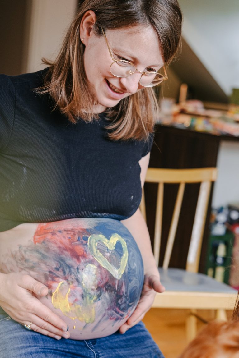 Kreatives bemalen von einem Bauch, bei einem Babybauchshooting.